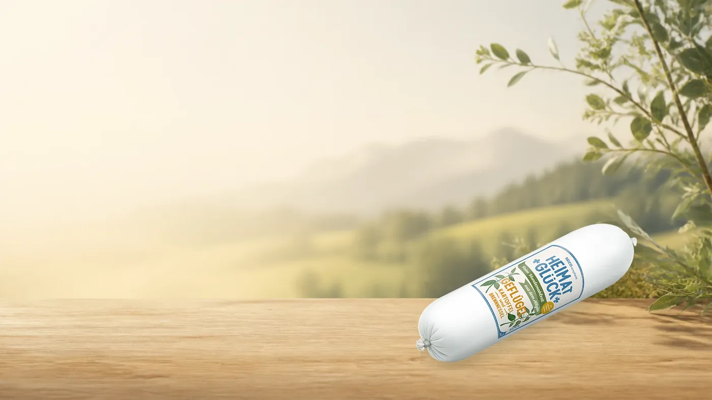 HEIMATGLÜCK Geflügel – offizielles REiCO Produktmotiv in warmer Naturkulisse mit heller Holzfläche.
