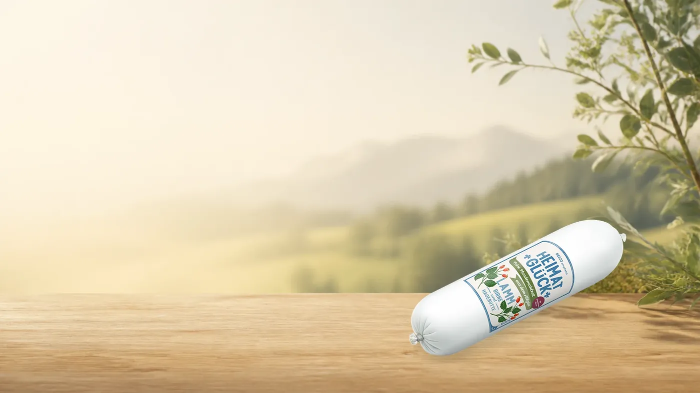 HEIMATGLÜCK Lamm – offizielles REiCO Produktmotiv in warmer Naturkulisse mit heller Holzfläche.